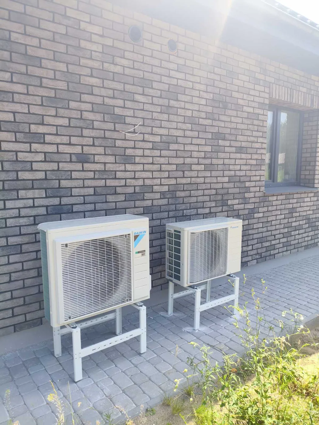 DAIKIN šilumos siurblio ir oro kondicionieriaus lauko blokai ant stovų prie mūrinio namo